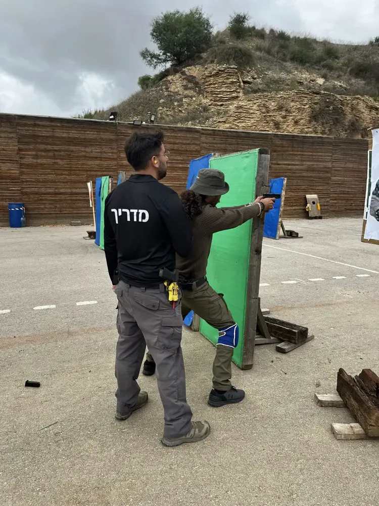 מדריך מלווה מתאמן בירי מאחורי מחסה במטווח הפתוח
